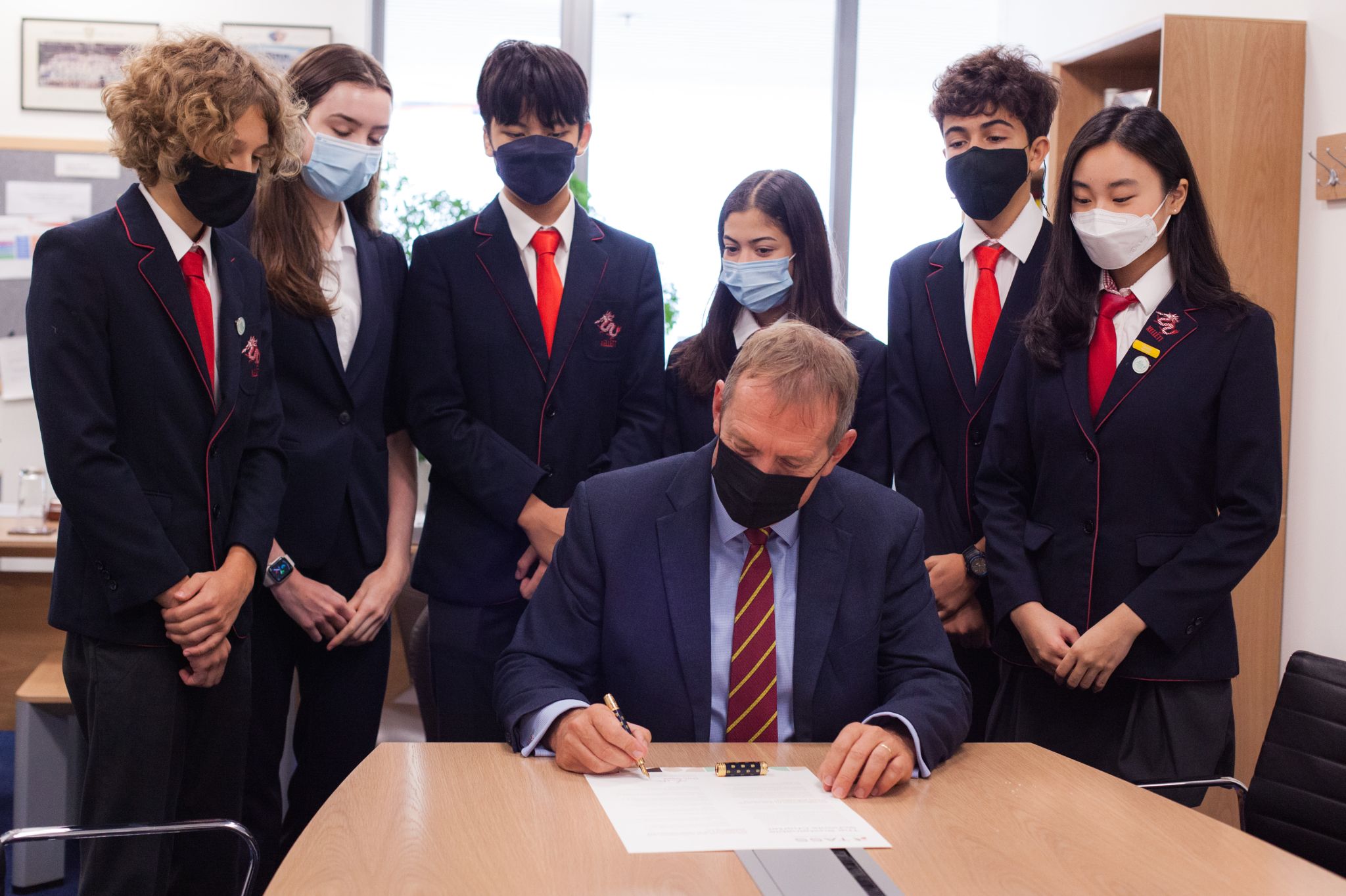 Photo of mark steed with students around him while he signs declaration 